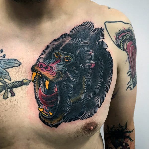 Bold baboon chest tattoo with a fierce open-mouthed expression, intricate fur detailing, and vibrant red and yellow accents for a powerful look.