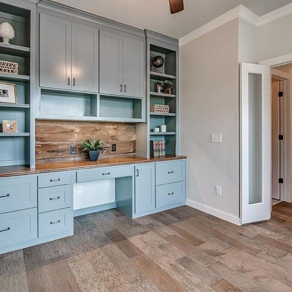 Home office with blue cabinets, a built-in desk, wooden countertop, and shelves; features a potted plant and wood flooring
