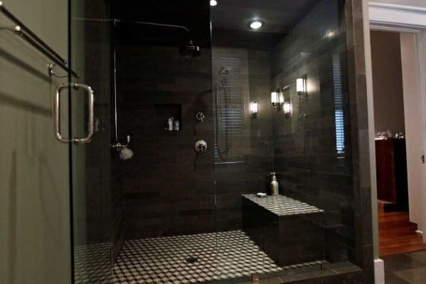 Dark-tiled walk-in shower with a glass door, bench, and rainfall showerhead