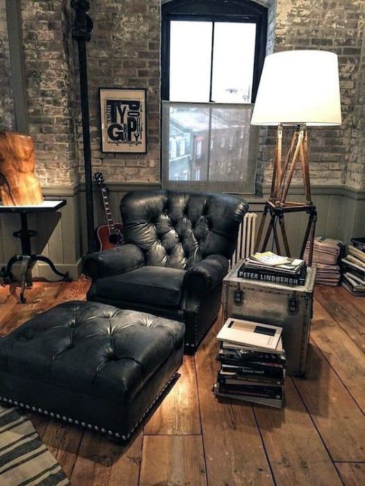 Black tufted leather armchair with matching ottoman in a cozy, rustic room with wooden floors and industrial decor.