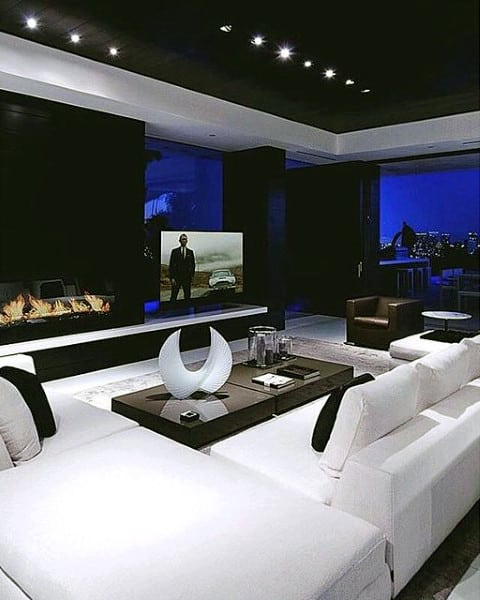 Modern living room with white sofas, a fireplace, a large painting, and a home theater overlooking the city skyline at night