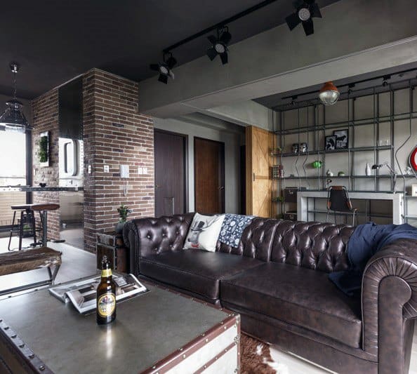 Modern industrial living room with a leather sofa, brick accents, and an open kitchen layout.