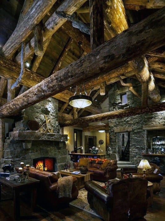 Rustic wood cabin living room with exposed beams, stone fireplace, and leather furniture.
