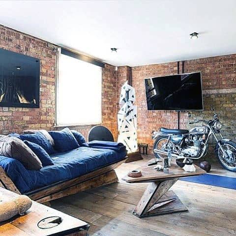 Living room with exposed brick walls, blue sofa, and a motorcycle as decor piece.