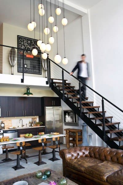 Stylish loft with open kitchen, leather couch, metal staircase, and modern pendant lighting.