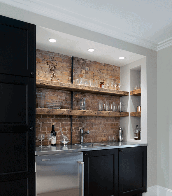 A small modern kitchen with brick backsplash, black cabinets, a bar area, stainless steel sink, and open wooden shelves