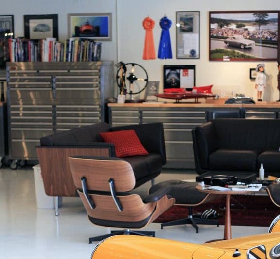 A stylish garage lounge with modern chairs, car memorabilia, and an orange car in the foreground