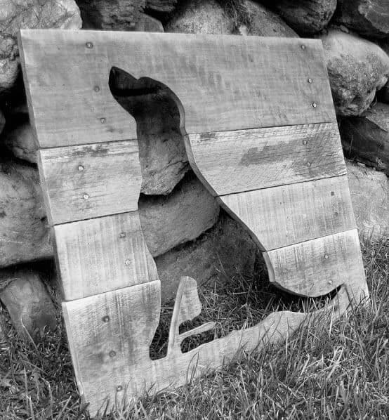 Wooden board with a dog silhouette cutout, leaning against rocks outdoors.