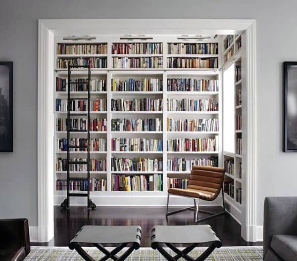 Large home bookshelf with sliding ladder and cozy reading chair in a dedicated nook.