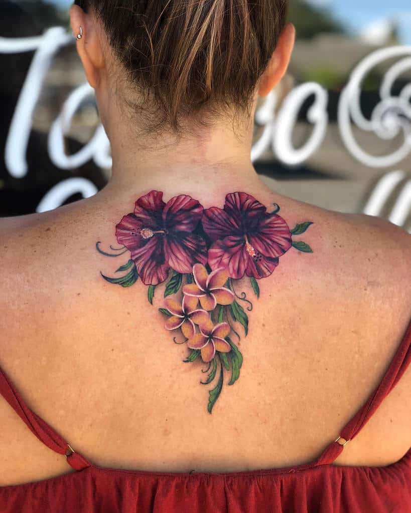 Back tattoo featuring a stunning arrangement of deep red hibiscus flowers combined with pink plumerias and green foliage, creating a vibrant tropical look