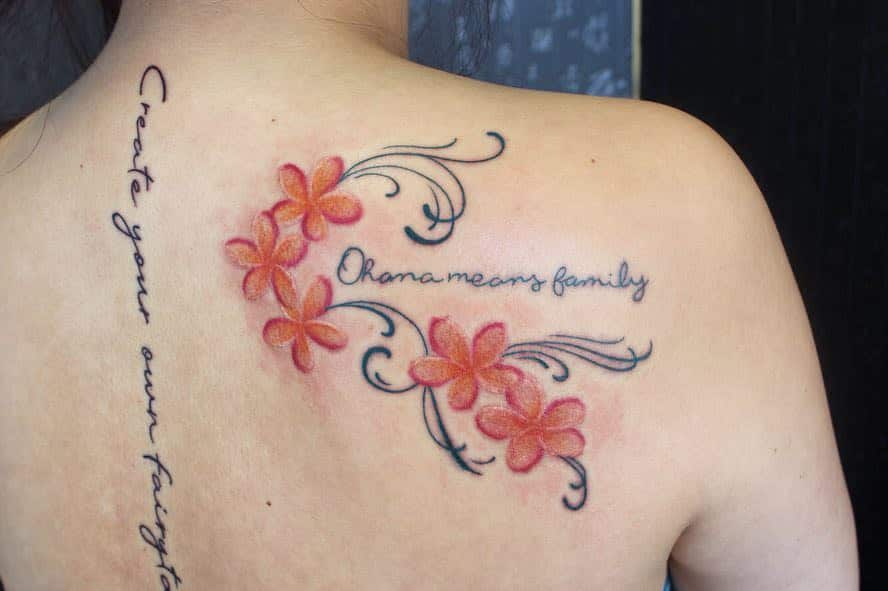 A vibrant back tattoo featuring delicate Plumeria flowers intertwined with elegant swirls, accompanied by the phrase 'Ohana means family' for a heartfelt design