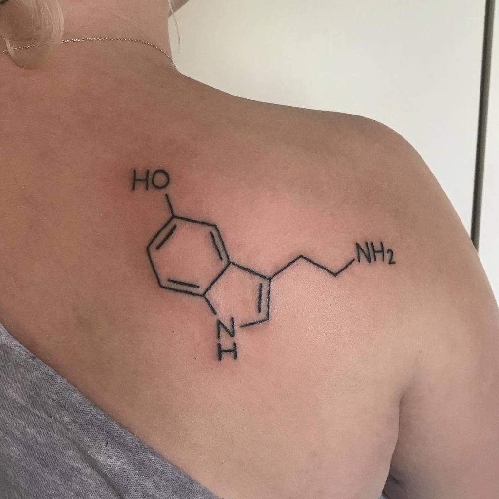 A delicate serotonin chemical structure tattoo graces the person's upper back, symbolizing joy and well-being in a subtle yet meaningful design