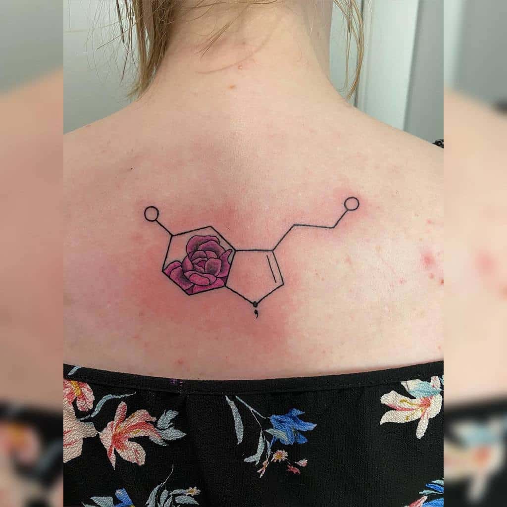 Tattoo of a serotonin molecule with a rose entwined within, elegantly etched on a woman's upper back