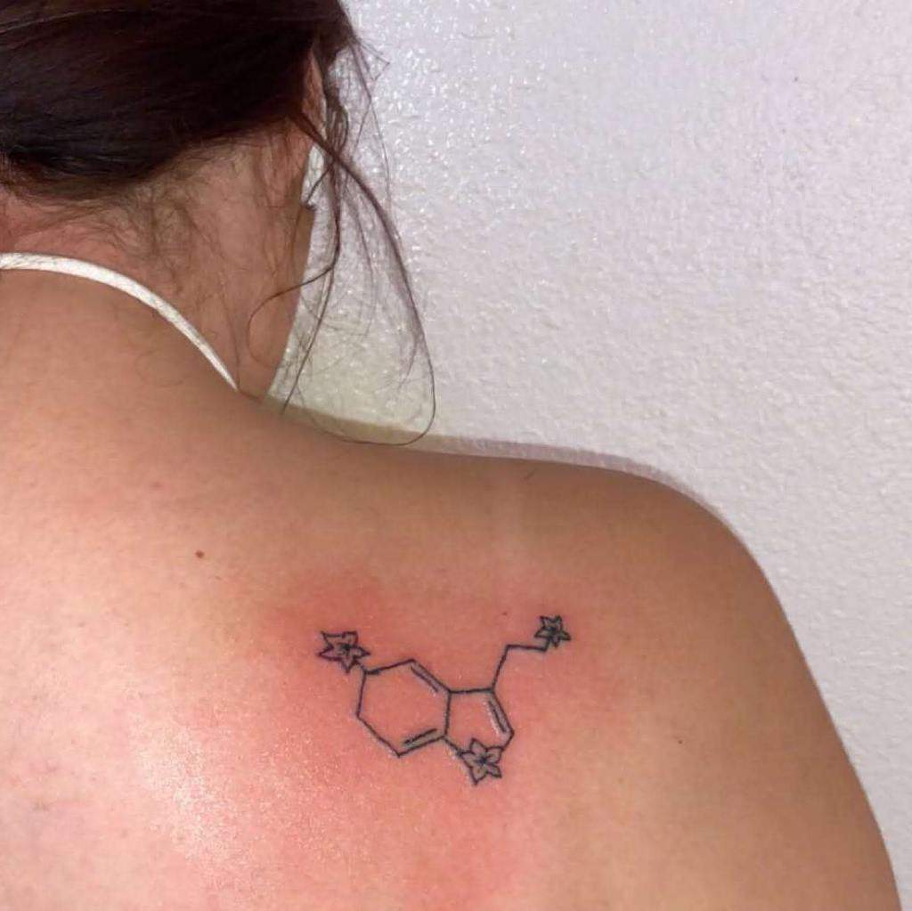 Tattoo of serotonin's chemical structure intertwined with flowers on a woman's upper back
