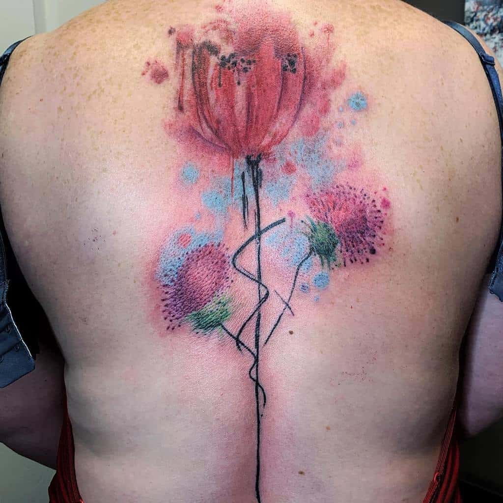 Watercolor-style tattoo of abstract thistle flowers delicately sprawled across a back