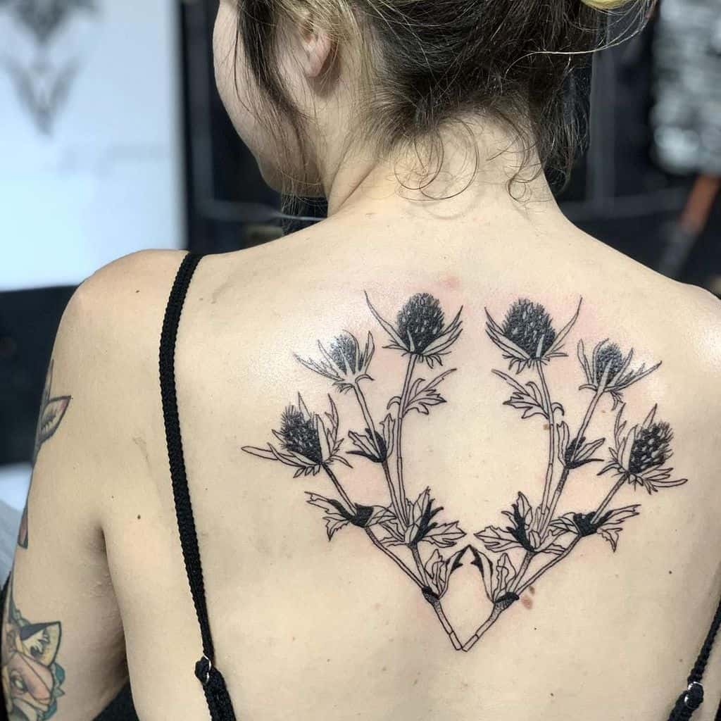 Elegant back tattoo featuring symmetrical black thistle branches with intricate leaf and flower details