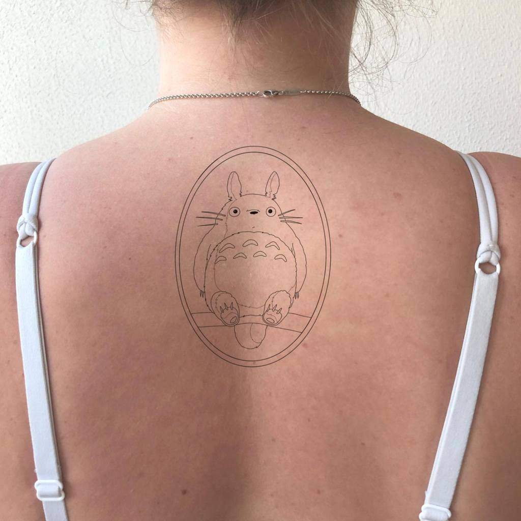 Minimalist Totoro tattoo on the upper back, enclosed in an oval frame, showcasing Totoro's iconic relaxed pose