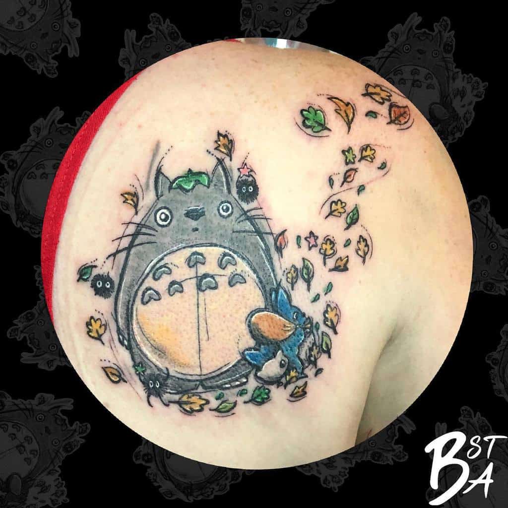 Whimsical Totoro tattoo on the shoulder, featuring Totoro surrounded by falling leaves, soot sprites, and smaller forest companions