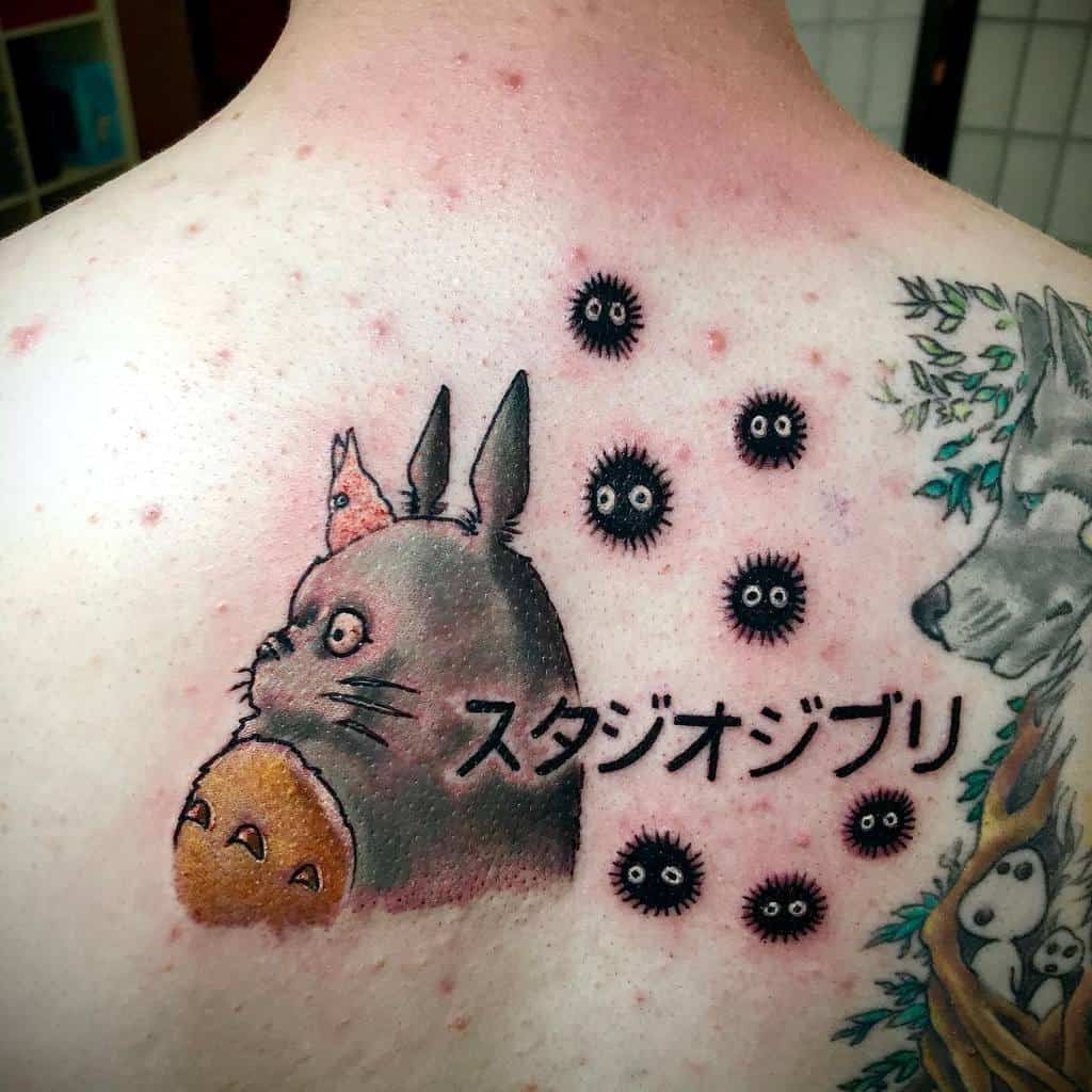 A stunning back tattoo showcasing Totoro with a thoughtful expression, accompanied by soot sprites and the Japanese characters for "Studio Ghibli"