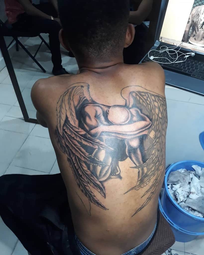 Black and grey tattoo of an angel covering his head into his arms depicting a fallen angel