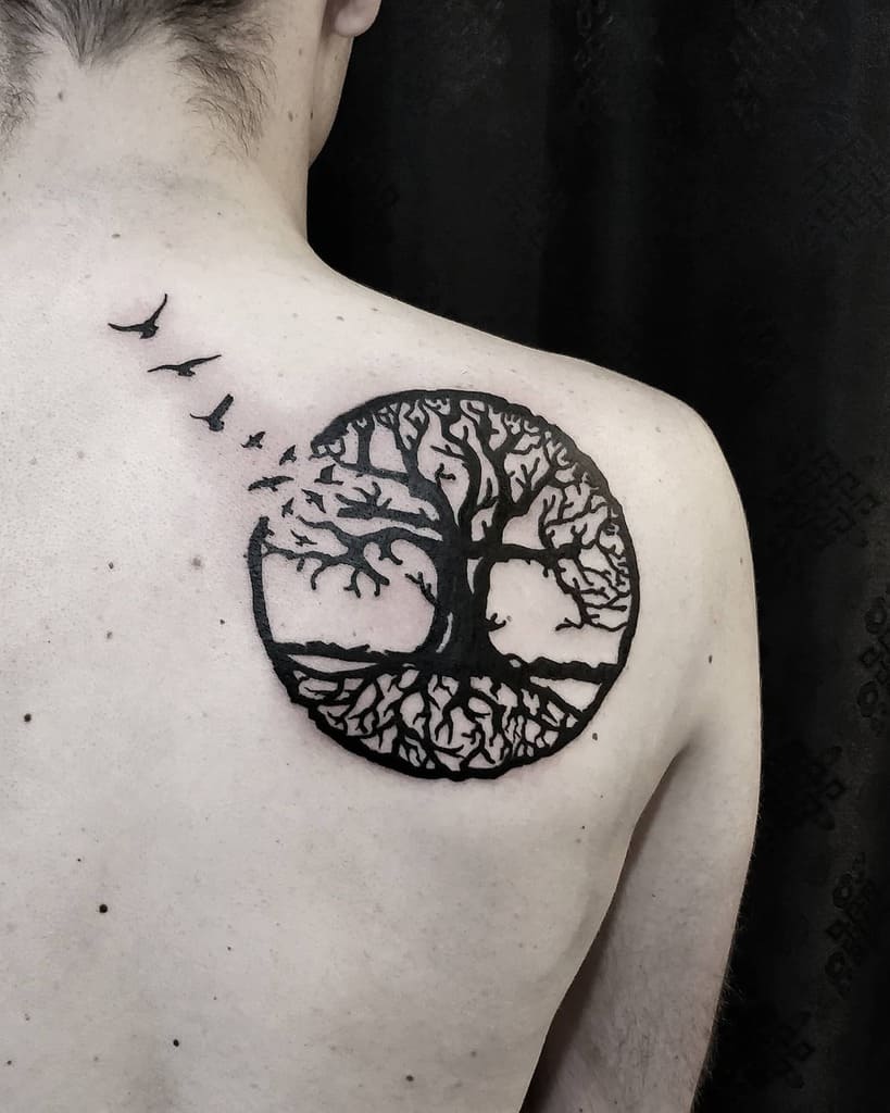 Bold back tattoo of a tree of life with intricate roots and branches in a circle, accompanied by birds in flight