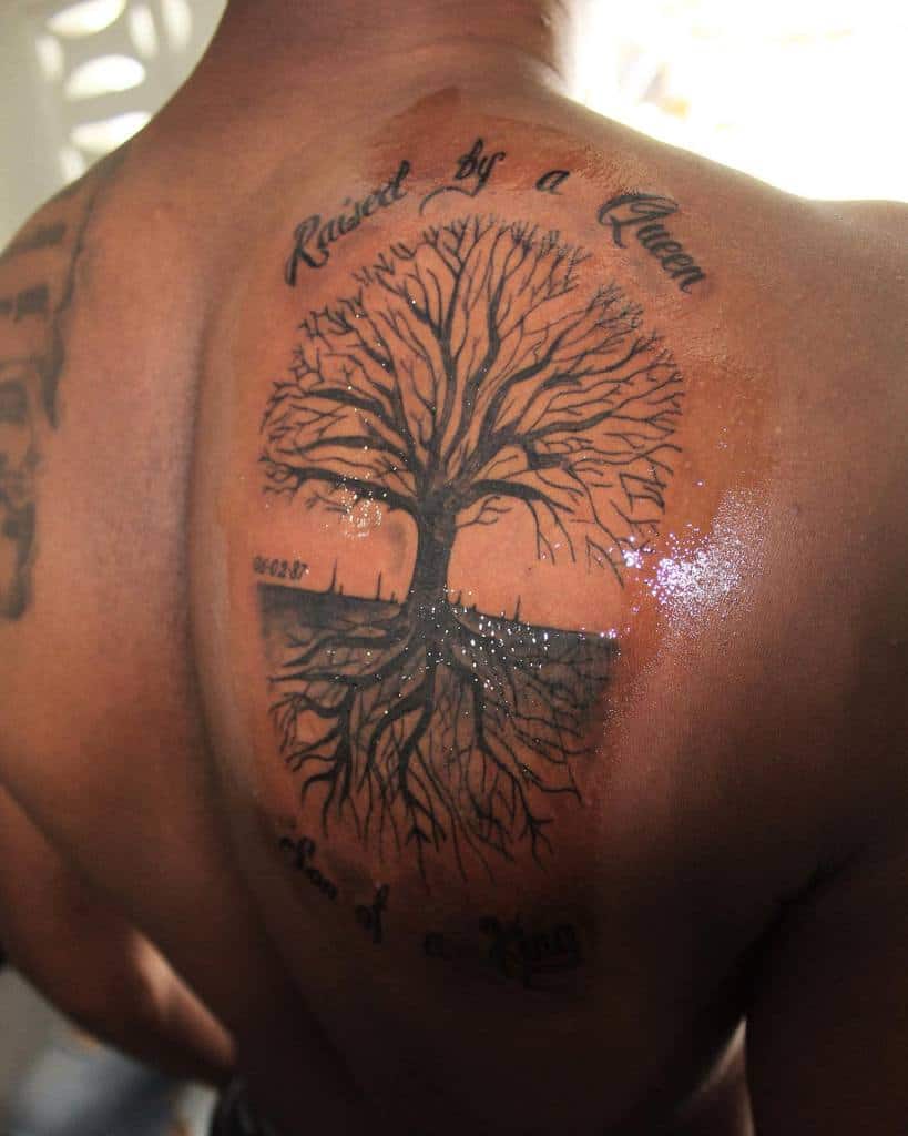 Back tattoo of a detailed tree of life with sprawling roots, featuring the text 'Raised by a Queen, Son of a King' above and below