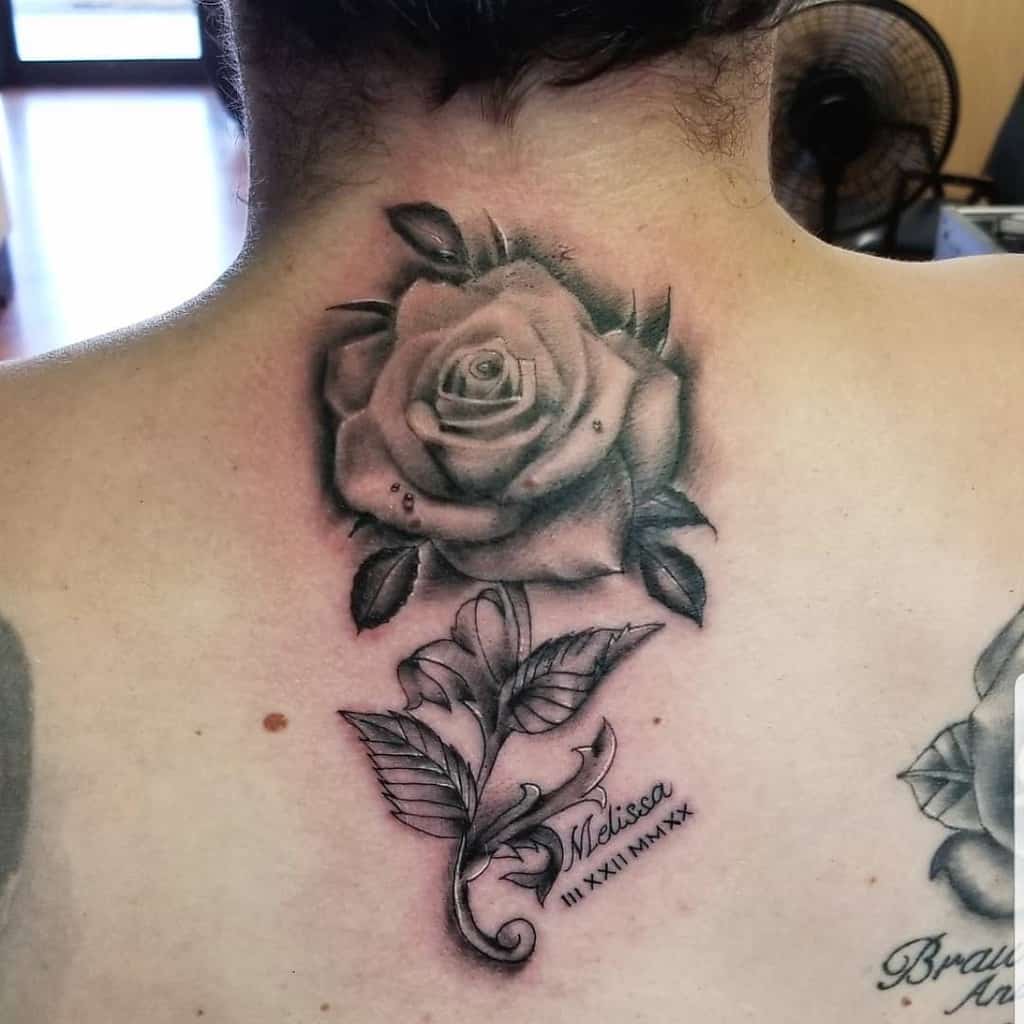 Tattoo of a shaded rose with leaves and the name "Melissa" on back