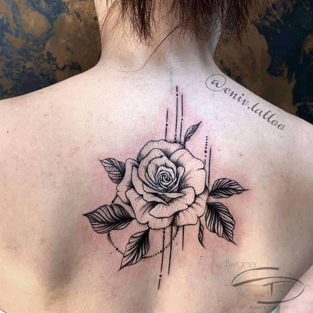 Back tattoo featuring a detailed black-and-white rose with artistic lines and leaf accents