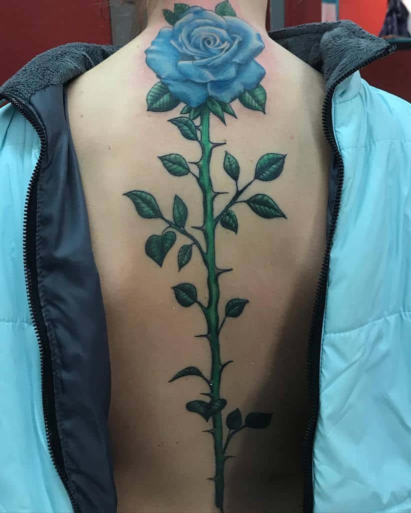 A striking tattoo adorns the person's back, featuring a large, vivid blue rose with a lush green stem and leaves