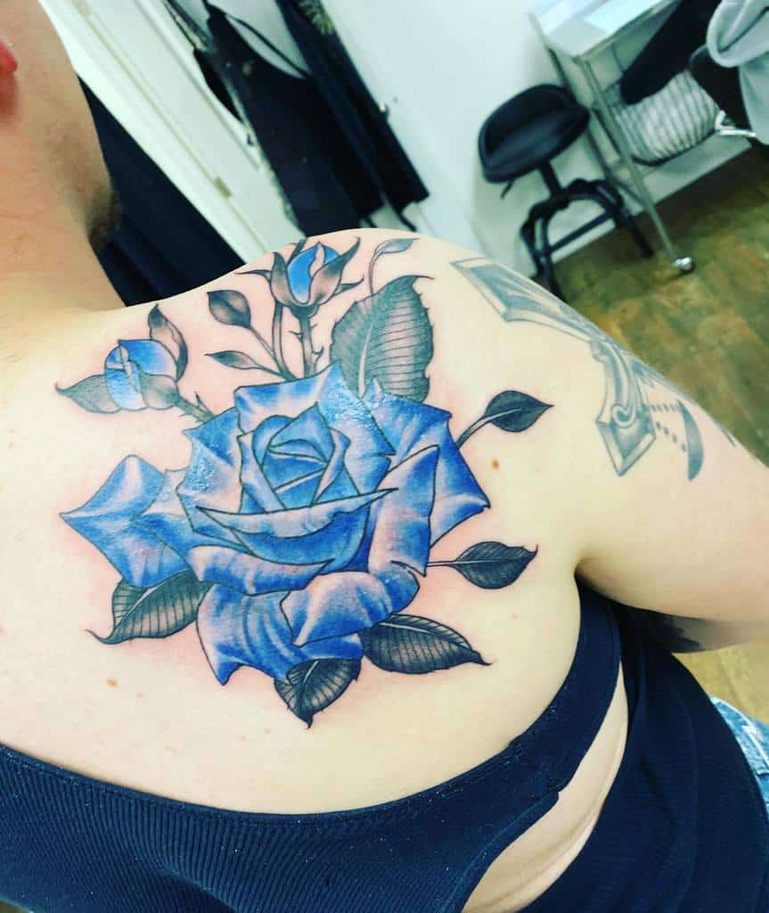 A blue rose tattoo graces the person's shoulder, complete with intricate leaves and buds