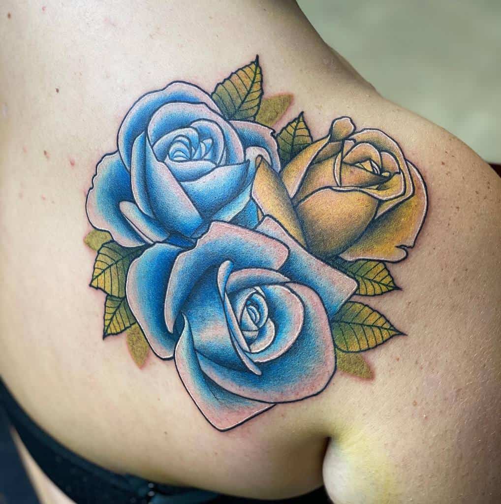 A vibrant tattoo of three roses in shades of blue and yellow, with green leaves, placed on the upper back near the shoulder