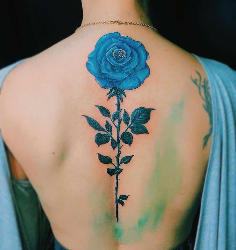 A large blue rose tattoo on the back, with intricate black shading on the stem and leaves, creating a striking contrast
