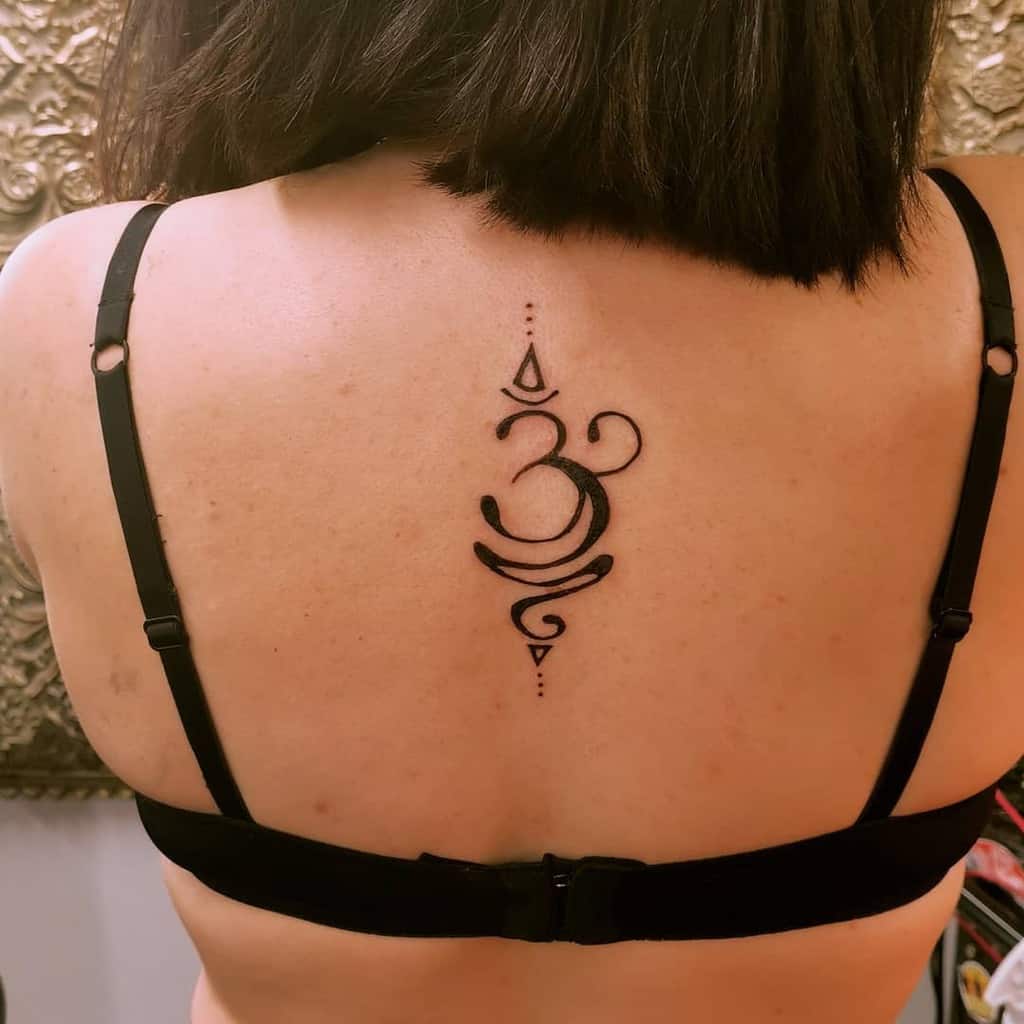 Om symbol tattoo centered on the upper back with geometric details and flowing curves, inked in bold black lines