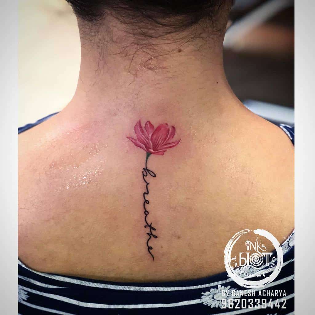 A delicate pink flower tattoo adorns the upper back, gracefully intertwined with the word "breathe," symbolizing tranquility and mindfulness