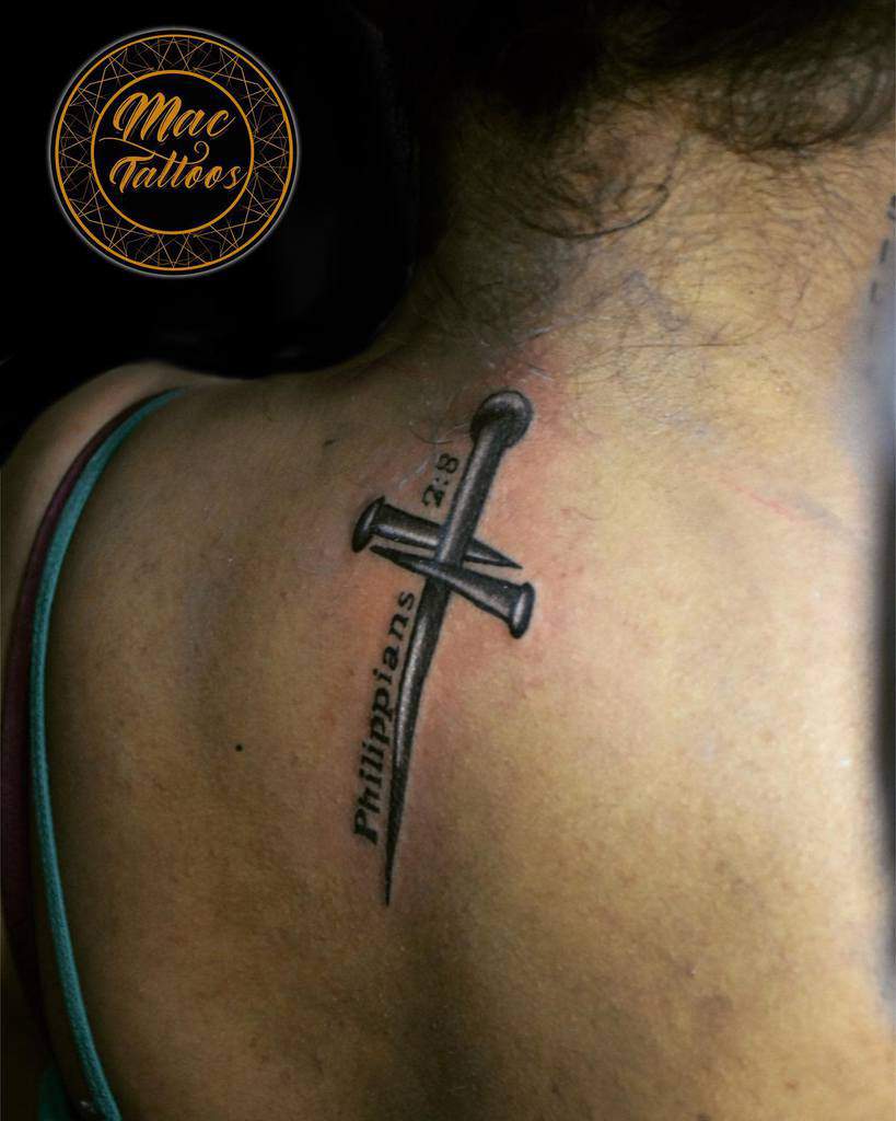 Tattoo of three nails elegantly forming a cross with "Philippians 2:8" etched on a person's upper back