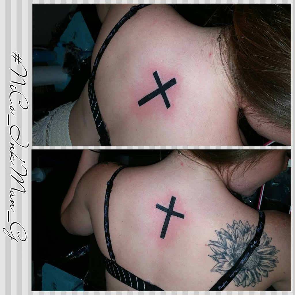 Black ink cross tattoo on woman's upper back