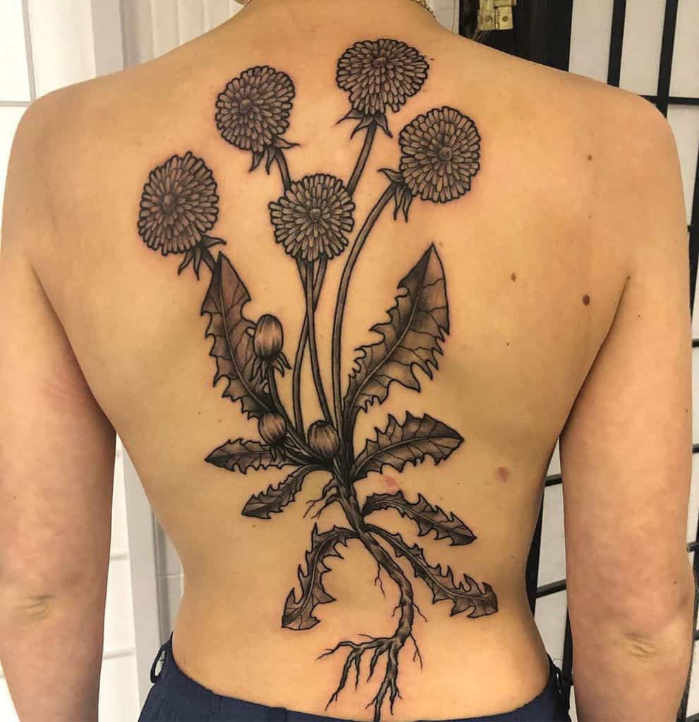 A bold black dandelion tattoo on the back, featuring multiple blooms and intricate roots extending down the spine.