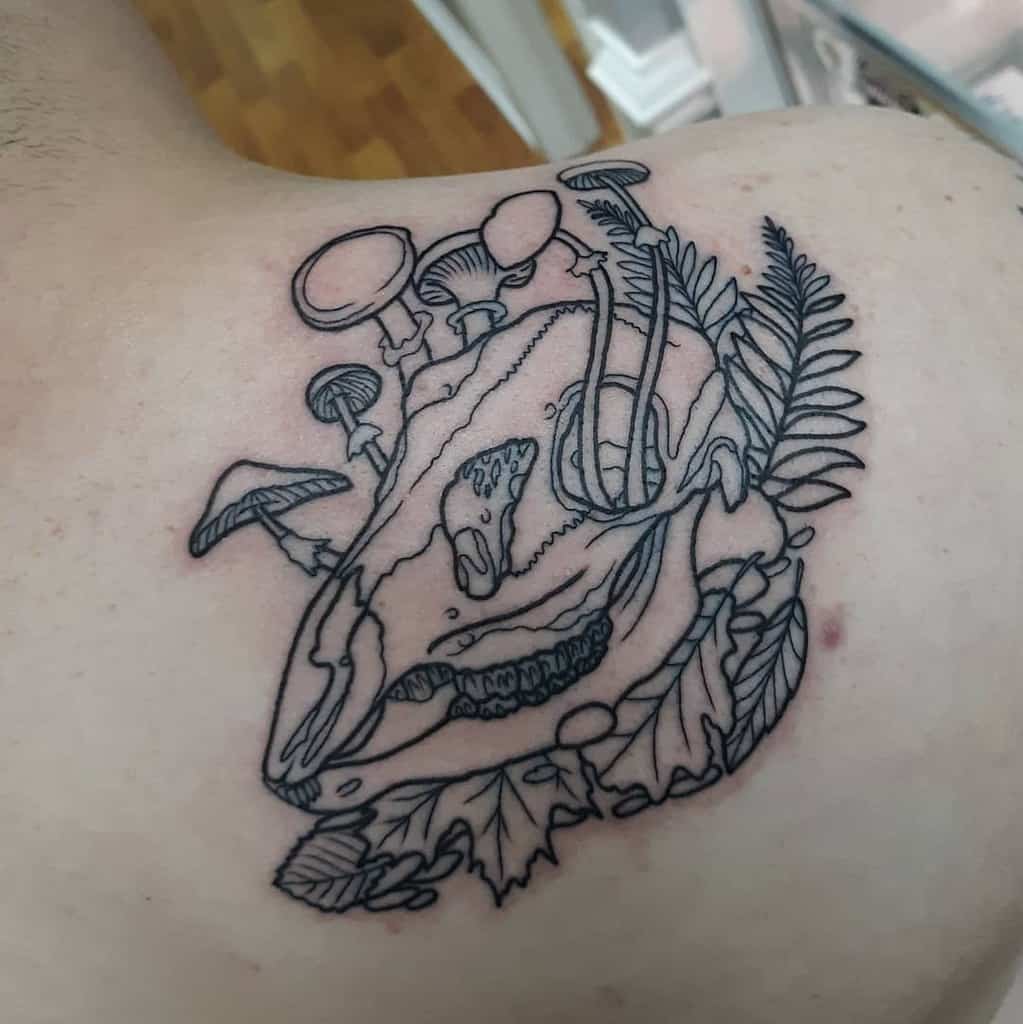 Line art tattoo of a deer skull with mushrooms and leaves on a shoulder