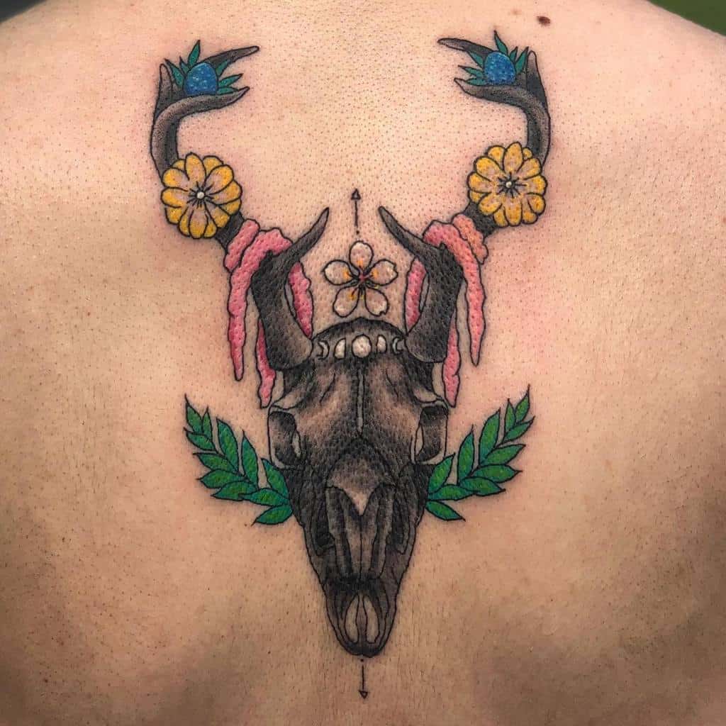 Artistic tattoo of a deer skull adorned with flowers and leaves, elegantly displayed on a back
