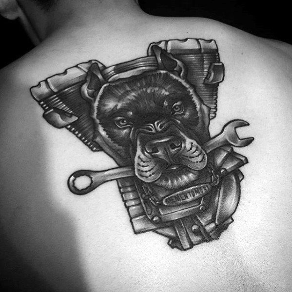 Black and grey tattoo of a pitbull with a wrench in its mouth, set against an engine block on the upper back.