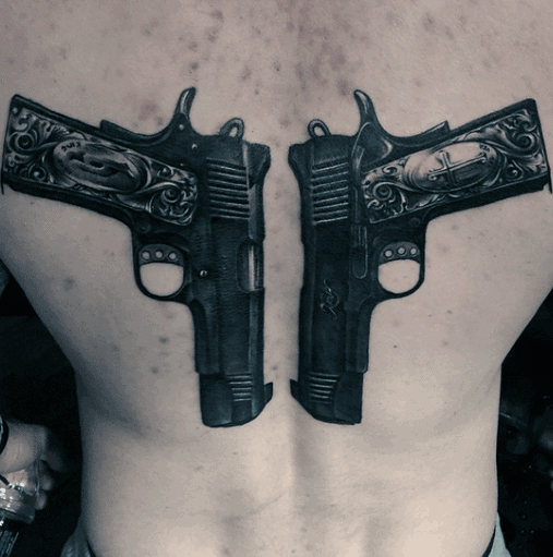 Black and gray back tattoo featuring two mirrored 1911 pistols with intricate engravings, creating a bold and symmetrical design.