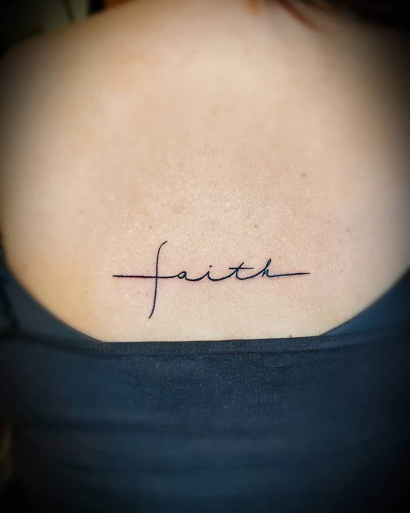 A minimalist "faith" tattoo in cursive graces the person's upper back, seamlessly incorporating a subtle cross into its elegant design