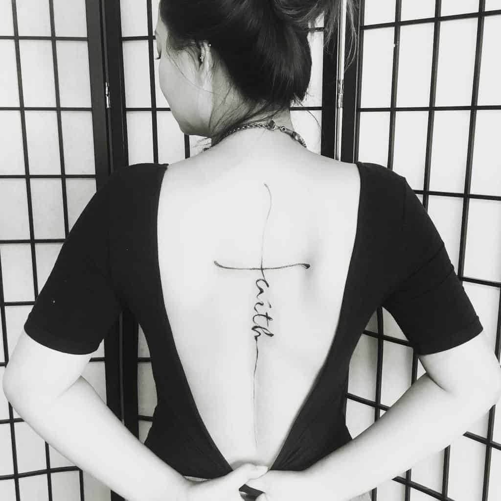Woman with a "Faith" spine tattoo, adorned with a small cross