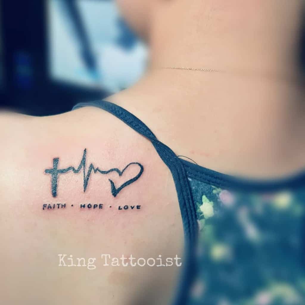 A shoulder tattoo elegantly featuring a cross, heartbeat, and heart captures the essence of "Faith - Hope - Love," blending these timeless values into a visual testament to life's enduring principles