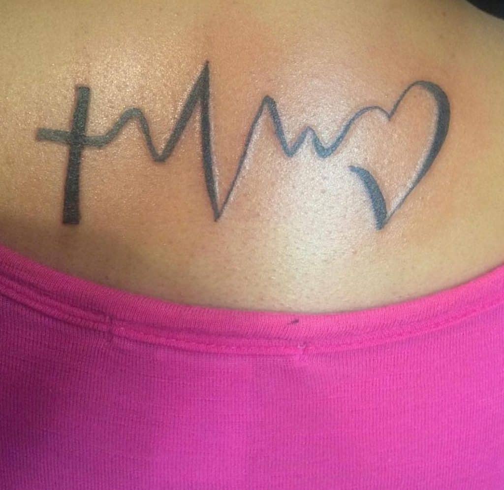 A tattoo of a cross, heartbeat line, and heart elegantly graces a person's upper back symbolizing faith, hope and love