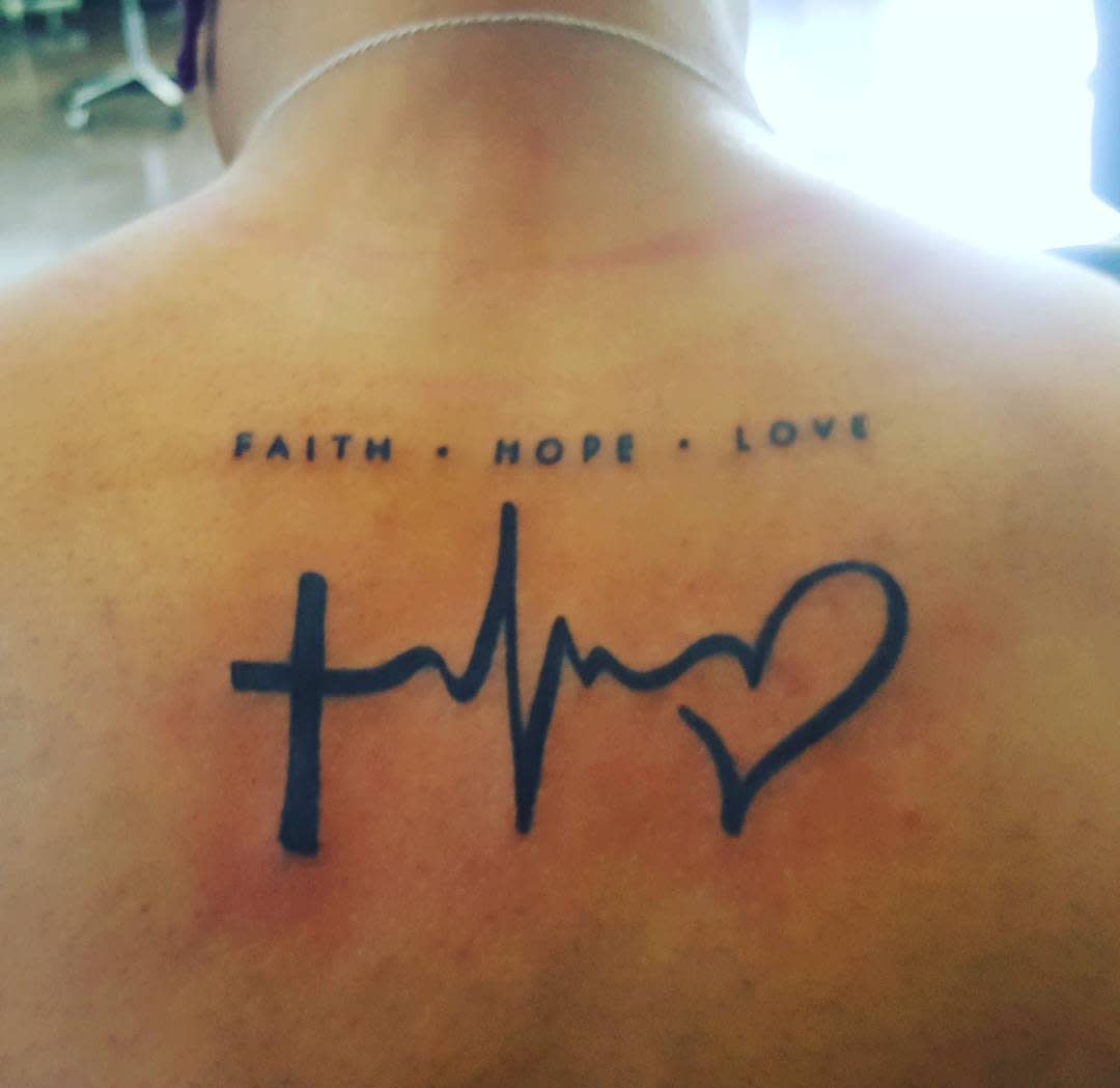 Back tattoo featuring a cross, heartbeat line, and heart elegantly intertwined under the powerful words "LOVE • HOPE • FAITH