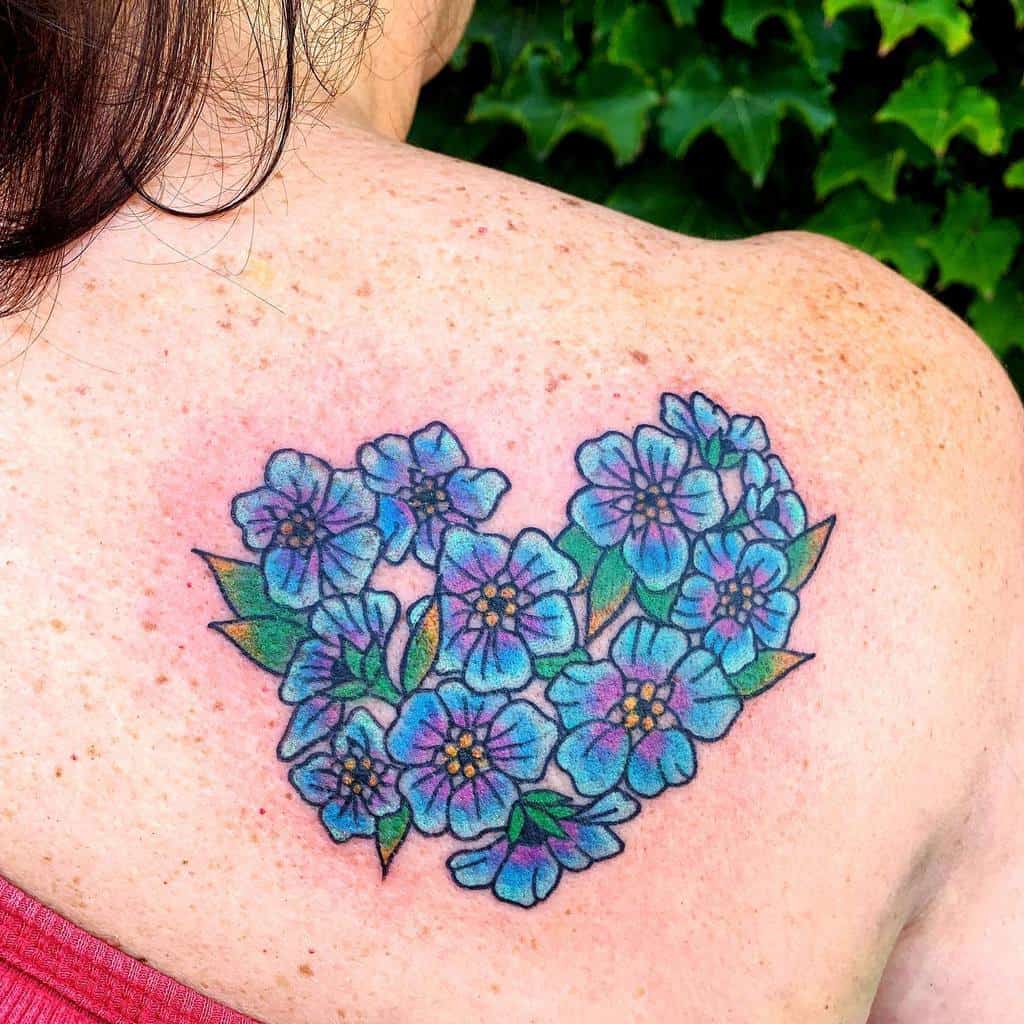 A heart-shaped floral tattoo featuring delicate blue forget-me-nots on a woman's back