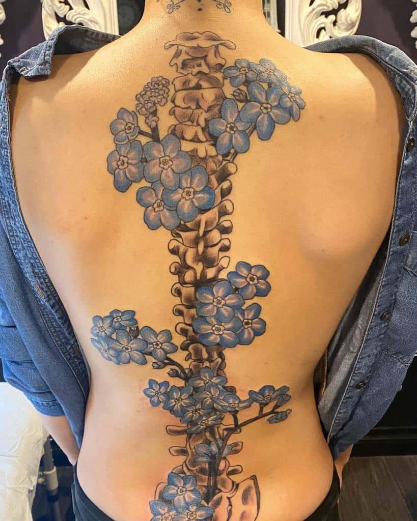 Tattoo of a spine adorned with delicate blue forget-me-not flowers on a back
