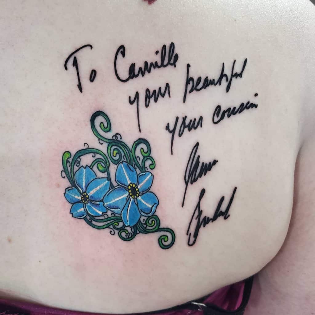 A tattoo of blue forget-me-not flowers and elegant handwriting graces a person's shoulder