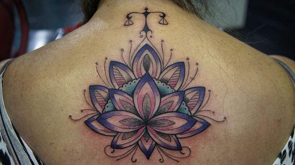 Mandala-inspired back tattoo with geometric petals in soft hues, accented by a delicate Libra scale symbol at the top